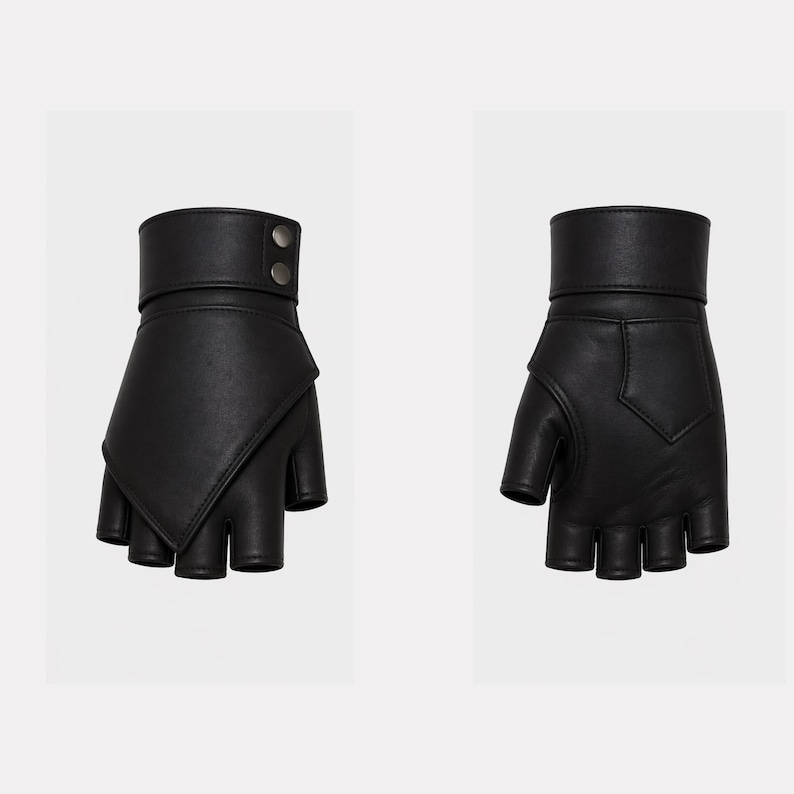 May include: A pair of black fingerless gloves made of leather. The gloves have a wrist strap with two silver-colored buttons. The design features a unique angled flap over the knuckles.