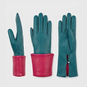May include: Three pairs of teal leather gloves with contrasting magenta cuffs. One pair is shown with the fingers extended, another with the hand open, and the third with a slit and button detail at the wrist. The gloves are displayed against a white background.