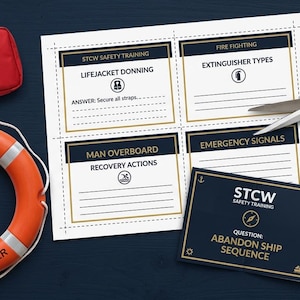 May include: A red first aid kit, an orange lifebuoy labeled STCW SOLAS M.V. SEAFARER, a sheet of STCW safety training cards with sections for lifejacket donning and fire fighting, a pair of metal scissors, and a red dry powder fire extinguisher.