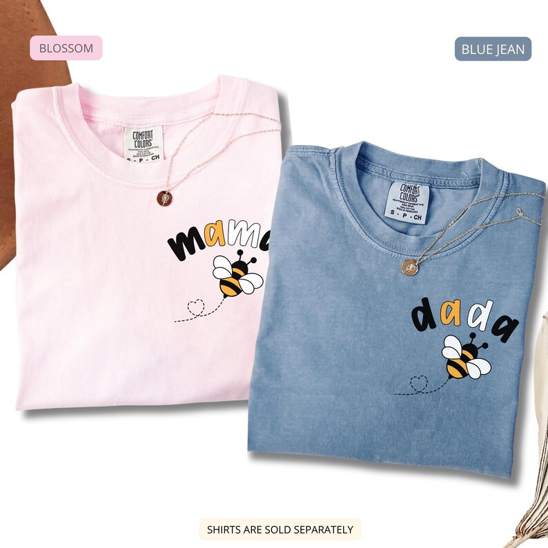 May include: Two short-sleeve crew neck t-shirts in blossom pink and blue jean colors. Each shirt features a graphic of a bee with a dotted flight path forming a heart, and the text mama on the pink shirt and dada on the blue shirt.