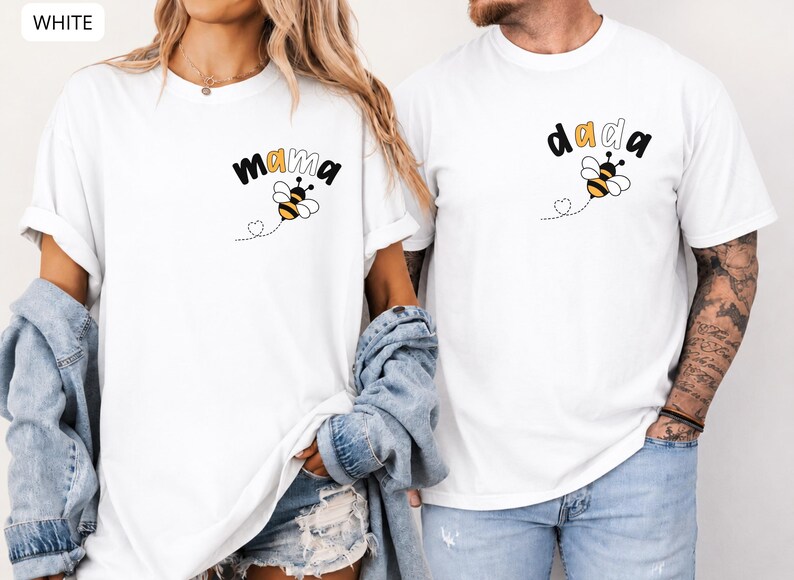 May include: Two white short-sleeve t-shirts featuring a small graphic on the left chest. One shirt displays the text "mama" with a bee illustration, and the other displays the text "dada" with a bee illustration. Both include a dotted heart trail.