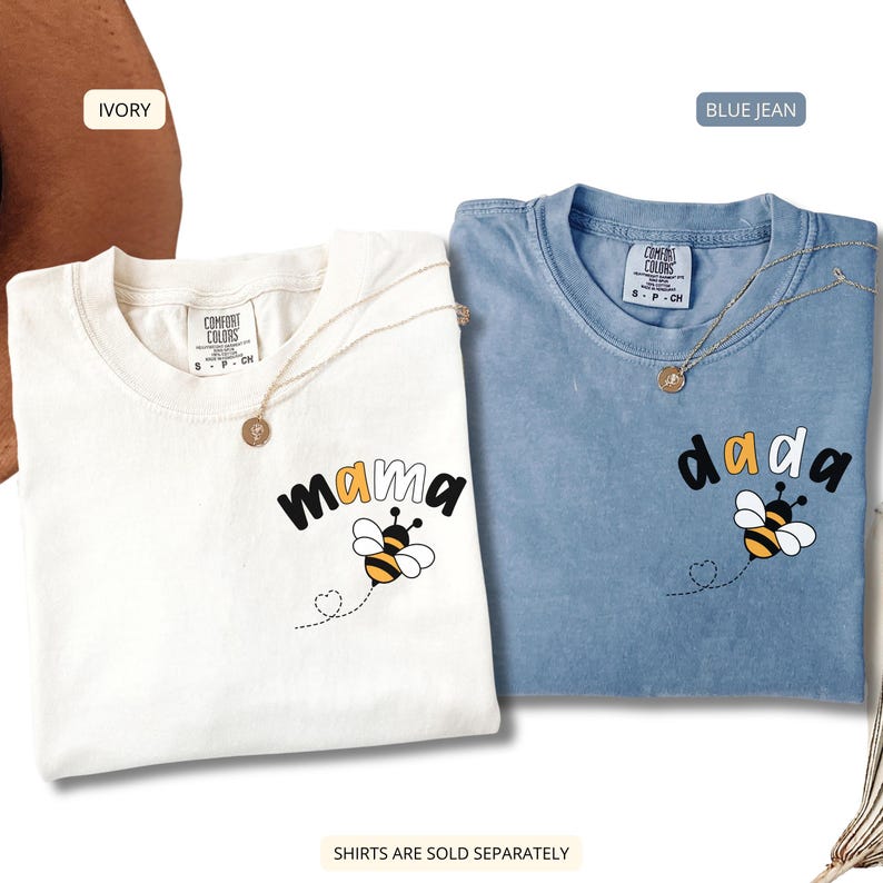 May include: Two short-sleeved t-shirts, one ivory and one blue jean, each featuring a graphic of a bee and the text 'mama' or 'dada' on the chest. The shirts have a Comfort Colors label at the inner neckline and a small heart-shaped flight path.
