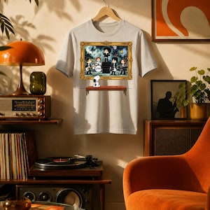 Könnte beinhalten: Ein hellgraues T-Shirt mit kurzen Ärmeln und einem Grafikdruck eines gerahmten Gemäldes. Das Kunstwerk zeigt eine Band, die im Cartoon-Stil auf einer Bühne auftritt, mit einem kleinen weißen Hund, der vor dem Rahmen auf einer Bank sitzt.