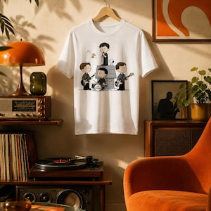 Peut inclure: Un t-shirt blanc à manches courtes orné d'une illustration graphique de quatre personnages de dessin animé jouant des instruments sur une niche, avec le texte Joy Division imprimé sur la batterie et Snoopy à proximité.