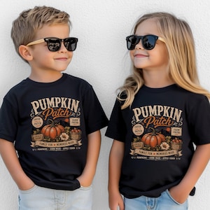 May include: Two black t-shirts featuring a graphic print with the text PUMPKIN PATCH, FRESH FROM THE PATCH, FARM FRESH, LOCALLY GROWN, FAMILY FUN MEMORIES MADE, PUMPKINS, CORN MAZE, APPLE CIDER, and an illustration of a pumpkin and autumn harvest.