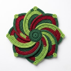 May include: A circular crochet coaster or trivet featuring a spiral pattern of alternating segments in dark green, lime green, and deep red yarn. The design radiates from a central circular point, creating a layered, pinwheel-like appearance.