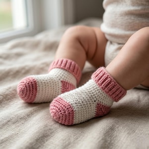 Può includere: Primo piano di due calzini da bambino. I calzini sono bianchi con dettagli rosa sulle dita e sui polsini. Sono realizzati in materiale a maglia. Questi calzini per bambini sono progettati per mantenere i piedini caldi.