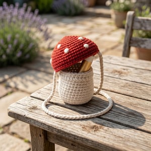 Peut inclure: Un sac en forme de champignon crocheté, avec un chapeau rouge et des pois blancs. Le sac a un corps de couleur crème et une bandoulière assortie. Le sac est posé sur une table en bois, mettant en valeur un design fantaisiste inspiré de la nature.