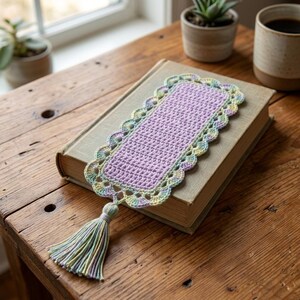 Peut inclure: Un marque-page rectangulaire au crochet avec un centre violet clair uni et une bordure festonnée en fil pastel panaché aux tons jaune, vert et bleu. Un pompon assorti aux couleurs variées est fixé sur le bord inférieur.