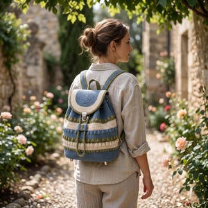 May include: A blue, cream, and green crochet backpack with adjustable straps and a drawstring closure. The backpack features a flap with a metal clasp and a decorative pattern. The bag is worn by a person walking on a stone path.