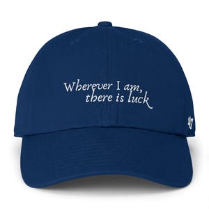 Puede incluir: Gorra de béisbol azul marino con la frase "Wherever I am, there is luck" en escritura blanca. El número "47" está bordado en el lateral. Un accesorio de moda.