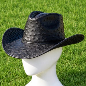 May include: A black cowboy hat featuring a distinct textured pattern of raised quill bumps across the entire surface. The hat has a structured crown with a central crease and a wide, curved brim, finished with a matching black band around the base.