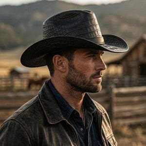 Puede incluir: Un sombrero de vaquero negro con un patrón texturizado de piel de cocodrilo en la copa y el ala ancha. El sombrero tiene una forma estructurada con una copa pellizcada y un ala curva, hecho de un material oscuro con acabado mate.