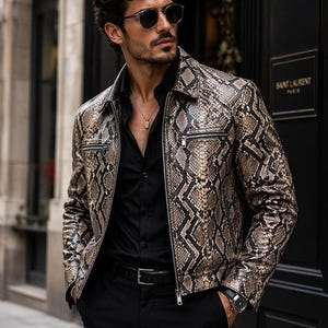 Peut inclure: Une veste à motif peau de serpent avec un imprimé d'écailles beige, marron et noir, un col pointu et des fermetures éclair en métal argenté sur les poches de poitrine et sur le devant. La veste est portée sur une chemise noire et un pantalon noir.