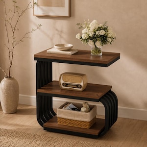 Op de afbeelding: Een bijzettafel met drie niveaus, donkerhouten planken en een gebogen zwart metalen frame. De bovenste plank bevat een witte kom en een boek, de middelste plank een vintage radio en de onderste plank een gevlochten mand.