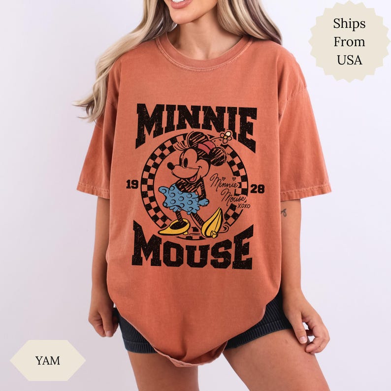May include: A rust-coloured t-shirt with a Minnie Mouse graphic. The design includes the text "MINNIE MOUSE" in black, with the years "1928" and "xoxo". Minnie Mouse is shown in a blue dress and yellow shoes, within a circular design.