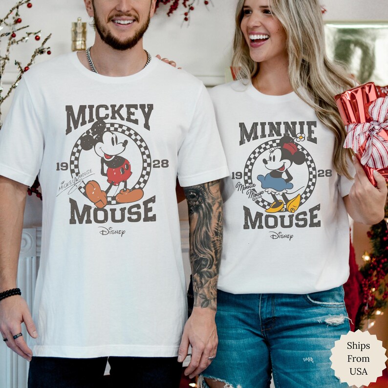 Puede incluir: Dos camisetas blancas de manga corta con gr&aacute;ficos de Disney de estilo vintage. La camiseta de la izquierda muestra a Mickey Mouse con el texto Mickey Mouse 1928. La de la derecha muestra a Minnie Mouse con el texto Minnie Mouse 1928, en c&iacute;rculos a cuadros.