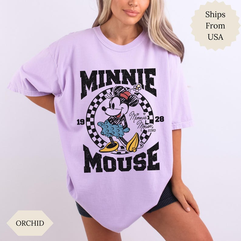 May include: Lilac t-shirt with a distressed Minnie Mouse graphic. The design features the text "MINNIE MOUSE" in black, with Minnie Mouse in the center. The shirt has short sleeves and a loose fit. The colour is described as Orchid.