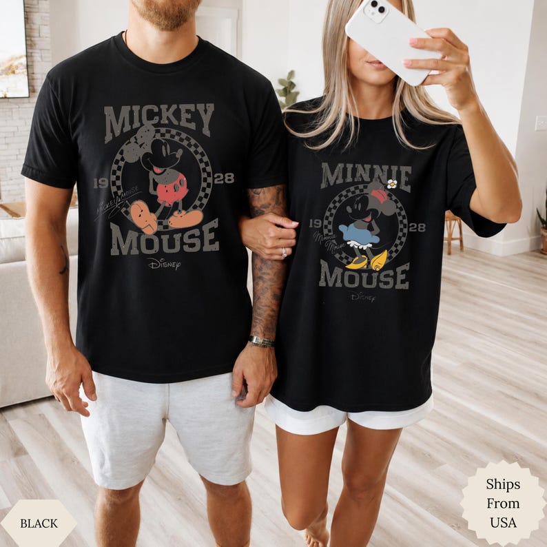 Puede incluir: Dos camisetas negras con estampados gr&aacute;ficos. La camiseta de la izquierda muestra a Mickey Mouse con el texto 'Mickey Mouse 1928'. La camiseta de la derecha muestra a Minnie Mouse con el texto 'Minnie Mouse 1928'. Ambos dise&ntilde;os incluyen un borde a cuadros.