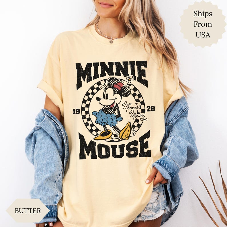 May include: A pale yellow t-shirt with a Minnie Mouse graphic. The design features the words "MINNIE MOUSE" in black, with "1928" and a checkered circle around Minnie. The t-shirt has a loose fit and rolled sleeves.