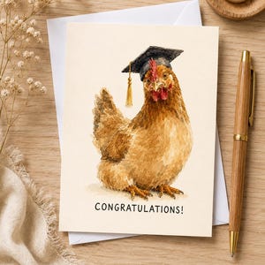 Op de afbeelding: Een wenskaart met een aquarelillustratie van een bruine kip die een zwarte afstudeerhoed met een gouden kwastje draagt. De tekst CONGRATULATIONS! staat in het zwart onderaan de crèmekleurige kaart die op een oppervlak is geplaatst.