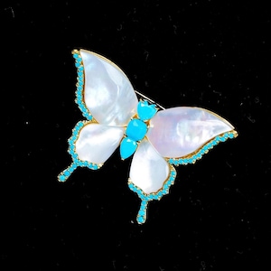 Peut inclure: Une broche en forme de papillon avec des ailes en nacre blanche irisée bordées de petites pierres turquoise vives. Le corps central du papillon se compose de trois segments turquoise lisses et éclatants montés sur une structure en métal doré.