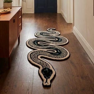 Peut inclure: Un long tapis sinueux en forme de serpent avec un corps à motifs noirs et crème, posé sur un parquet en bois sombre dans un couloir. Le tapis présente une tête détaillée, un corps courbé et une langue fourchue, créant un point focal au sol.