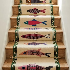 May include: A cream-colored stair runner with a green geometric border and a repeating pattern of multi-colored fish. The runner is secured to wooden stairs with brass stair rods and features a fringed edge at the bottom of the staircase.