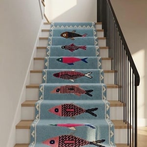 May include: A light blue stair runner carpet featuring a repeating pattern of stylized fish in various colors including brown, pink, and orange. The runner has a white geometric border and a fringed edge at the bottom, covering wooden stairs.
