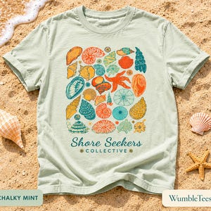 Op de afbeelding: Lichtgroen t-shirt met een kleurrijke schelpenafbeelding. Het ontwerp bevat diverse schelpen, een zeester en de tekst "Shore Seekers Collective". Het shirt is gemaakt van zacht materiaal.