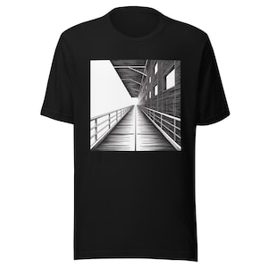 May include: A black short-sleeve t-shirt featuring a centered square graphic print. The illustration depicts a perspective view of a long wooden walkway with railings, leading toward a modern building structure with windows under a roof overhang.