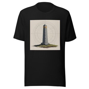 May include: A black short-sleeved t-shirt featuring a centred graphic of a grey stone obelisk standing on a small patch of green grass. The obelisk has two circular gold accents near the top, set against a background of thin, circular lines.