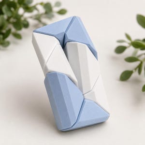 Può includere: Un giocattolo puzzle geometrico nei toni del celeste e del bianco. Il giocattolo è composto da diversi pezzi triangolari e rettangolari che si incastrano per formare una forma rettangolare. Il puzzle è progettato con un'estetica moderna ed è adatto a tutte le età.