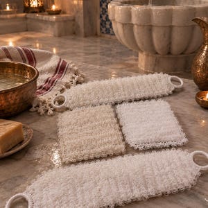 Puede incluir: Un conjunto de cuatro accesorios de baño en color blanco y blanco roto que incluye dos estropajos de espalda rectangulares largos con asas circulares en los extremos y dos almohadillas rectangulares más pequeñas, todos con una textura de malla sintética.