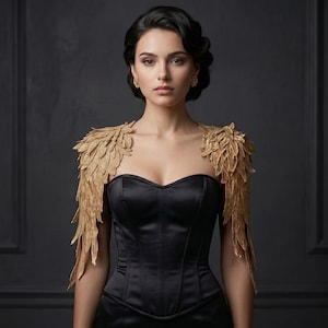 Può includere: Un top a corsetto nero senza spalline con intricati inserti dorati sulle spalle che ricordano ali piumate. Il capo presenta un corpetto strutturato con scollo a cuore e una finitura liscia simile al raso, abbinato a orecchini dorati.