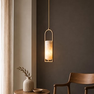 Puede incluir: Una lámpara colgante cilíndrica con una pantalla de piedra de brillo cálido suspendida por un marco de metal dorado. El accesorio presenta un diseño vertical con un arco superior redondeado, emitiendo una luz suave hacia abajo.