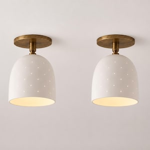 May include: Two flush mount ceiling lights featuring dome-shaped white shades with small perforated holes that allow light to pass through. Each fixture has a circular antique brass canopy and a matching brass stem connecting to the shade.