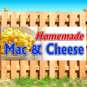 May include: A rectangular banner featuring a white background with the red text Homemade and the blue text Mac & Cheese. To the left, a white bowl is filled with yellow macaroni and cheese. The banner has metal grommets in each corner.