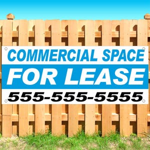 May include: A rectangular white vinyl banner with blue horizontal stripes and bold text that reads COMMERCIAL SPACE FOR LEASE followed by the phone number 555-555-5555. The banner features metal grommets in each corner for mounting purposes.