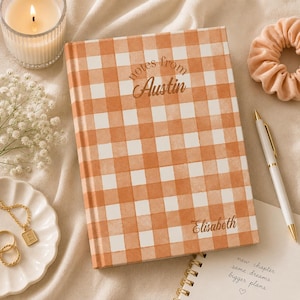 May include: A hardcover notebook with a white and orange gingham pattern. The cover features the text "notes from Austin" in a script font and the name "Elisabeth" printed in the bottom right corner in a matching script font.