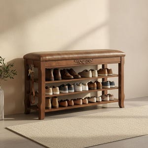 May include: A wooden shoe storage bench with a brown upholstered seat and three open shelves. The frame features carved detailing on the front apron. A set of keys hangs from a hook on the left side of the bench, which is filled with various shoes.
