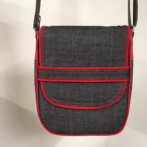 May include: A dark blue denim crossbody bag with red stitching and a flap closure. The bag has a single strap and a small pocket on the front.