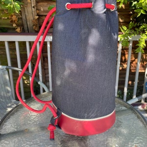 May include: A red and gray drawstring bag with a red drawstring and silver eyelets. The bag is sitting on a glass table.