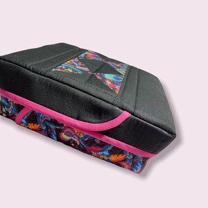 Puede incluir: Una caja de almacenamiento acolchada negra con un borde rosa y un patrón floral colorido en la parte inferior.