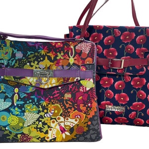 May include: Two colorful fabric handbags. The first handbag has a black background with a colorful floral and butterfly pattern. The second handbag has a navy blue background with a red poppy pattern. Both handbags have a purple leather strap and a silver buckle.