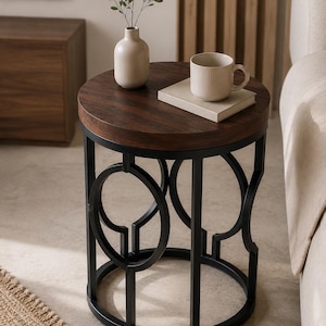 May include: A round side table with a dark brown wood grain top and a black metal base featuring a geometric circular frame design. On the table sits a beige ceramic vase with a small green plant, a light-colored book, and a beige ribbed mug.