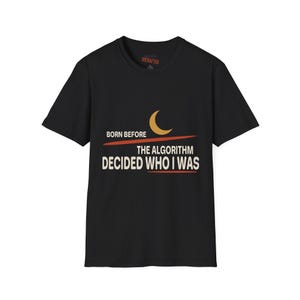 May include: A black short-sleeve t-shirt featuring a graphic design with a yellow crescent moon and orange horizontal lines. The text reads: BORN BEFORE THE ALGORITHM DECIDED WHO I WAS. The shirt has a crew neckline and a standard fit.