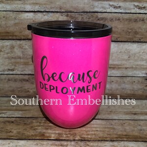 May include: Pink tumbler with a black lid and the text "because deployment" in black lettering. The tumbler is decorated with glitter.