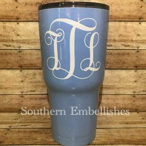May include: A light blue tumbler with a white glitter finish and a white monogram "JL" on the front. The tumbler is on a wooden background. Southern Embellishes is written in black text at the bottom of the image.