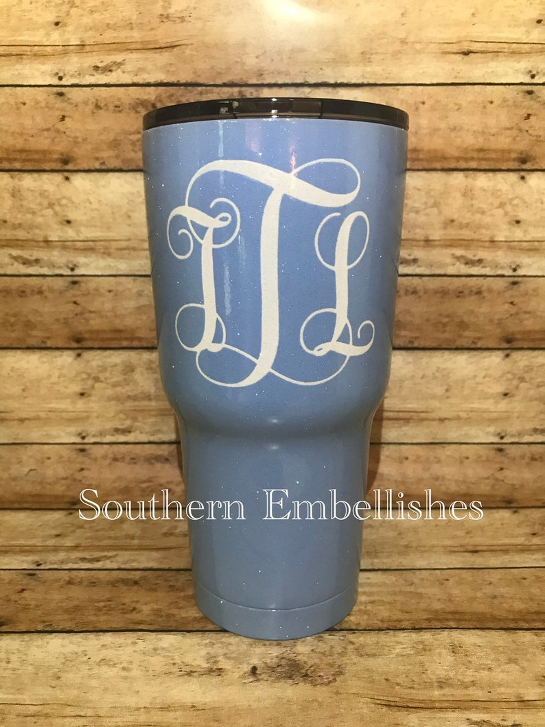 May include: A light blue tumbler with a white glitter finish and a white monogram "JL" on the front. The tumbler is on a wooden background. Southern Embellishes is written in black text at the bottom of the image.